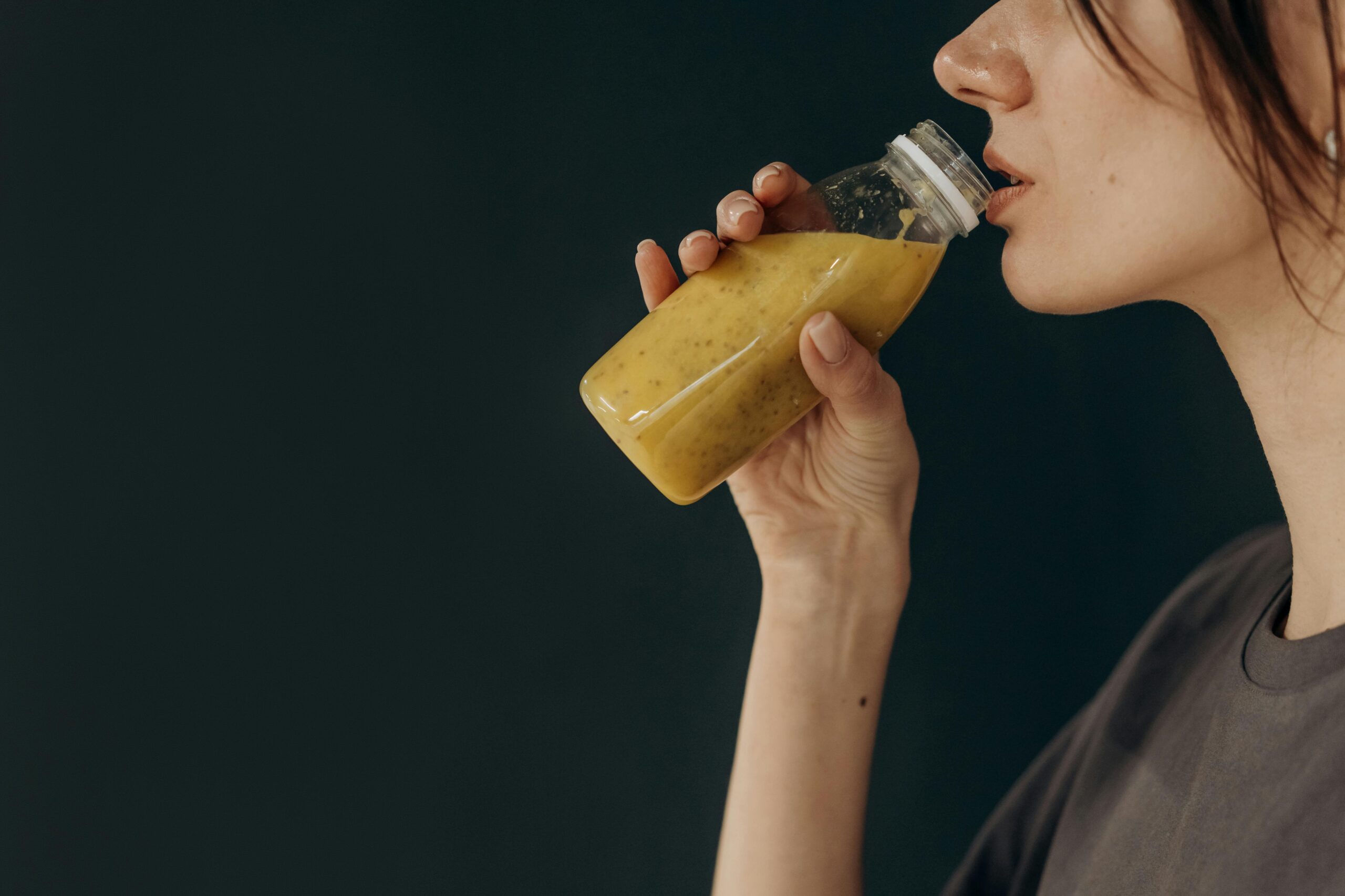 Side profile of a young woman sipping a nutritious smoothie from a bottle, showcasing a healthy lifestyle.